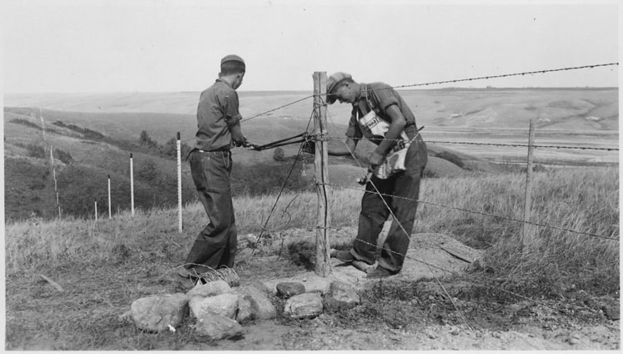 Two men string barbed wire on post to create a fence, circa 1936.